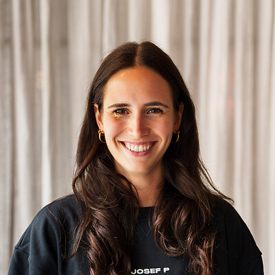 Frau mit langen, dunklen Haaren trägt einen schwarzen Pullover mit dem weißem Schriftzug "Josef P".