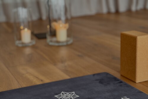 Matte mit dem Schriftzug "DAS EDELWEISS" auf Holzboden vor einem beigen Vorhang und Kerzen.