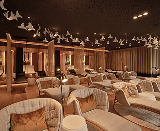 Gemütlicher Ruheraum mit gepolsterten Liegen, kleinen runden Tischen und hängenden weißen Dekorationen an der Decke.