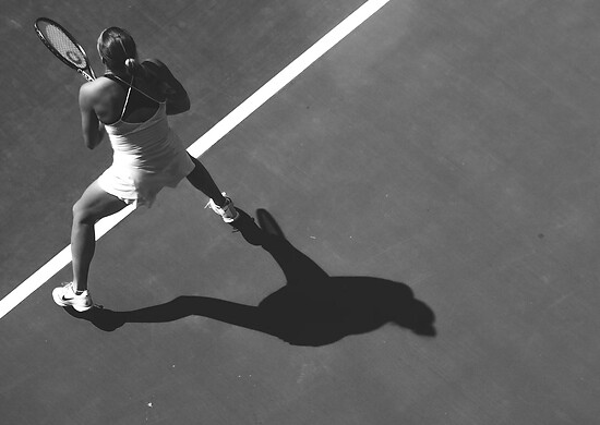 Schwarz-weiße Luftaufnahme einer Tennisspielerin in Aktion nahe einer Spielfeldlinie.