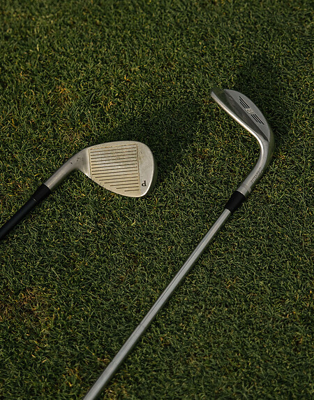 Zwei Golfschläger liegen auf grünem Rasen - auf der Schlagfläche sind sichtbare Rillen.